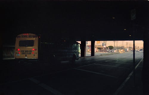 Photograph of a bus driving through a dark underpass, back end illuminated and the end of the underpass visible, showing an auto shop and street.