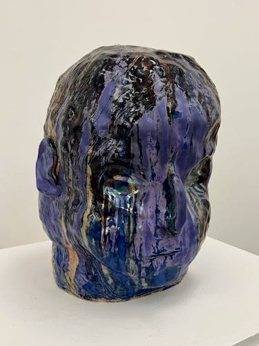 A large ceramics purple head, glazed with a combination of matt, shiny and metalic glazes dripped from the top of the head.