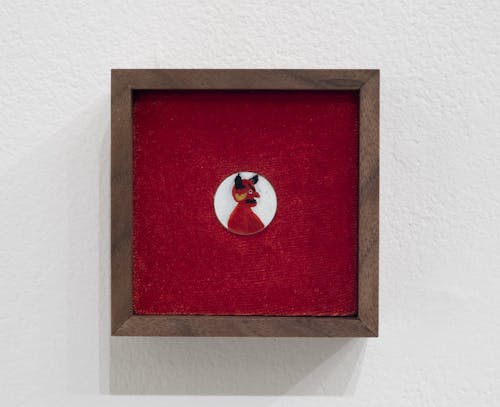 A small devil painted onto a USD penny, pressed into a bed of velvet in a walnut frame