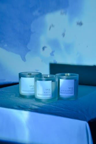 Three candles inspired by Sage Hill with labels in white. Photographed against a blue cyanotype of flowers.