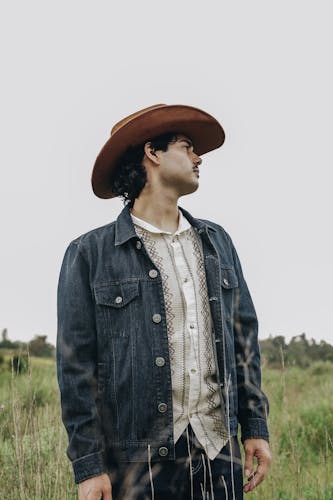 Male sitting in a field with vaquero attire and hat