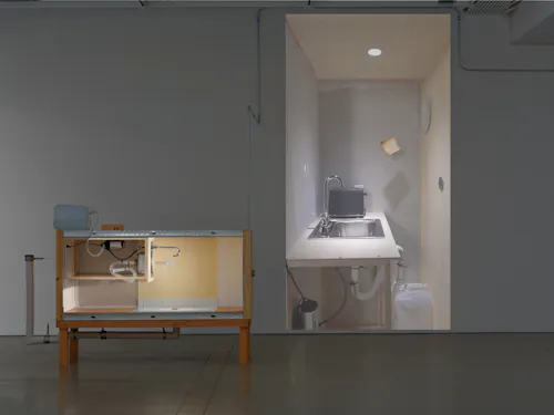 The Disoriented Room (2025). Mixed media installation with drywall, wood, porcelain, plumbing, wallpaper, lighting, and video projection. Dimensions variable.