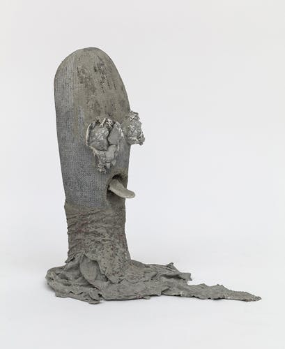 A concrete figure cast in a ski mask stands about 2 feet tall. It has concrete lace fabric around its bottom half, a concrete tongue sticking out of its mouth, and its eye's are busted open - still protruding but revealing broken stone. 