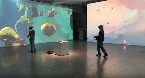 An image of two audiences playing VR games. The game is being projected on the three sides of the room.