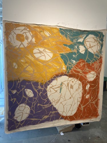 A large 72 inch by 72 inch painting with four main colors covering a section of the paintings. It is covered by a flesh colored caged.