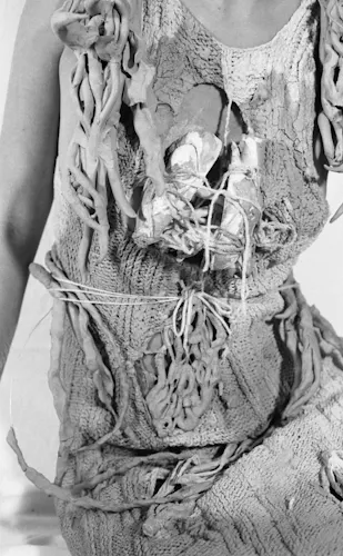 A ceramic aand wool knit dress is pictured as a black and white image. There are several protruding ceramic pieces coming from the dress. The dress is on a person, and the person is leaning slightly towards the viewer.
