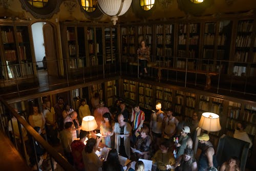 Still photograph of 40 guests in a library full of books, taken from a balcony