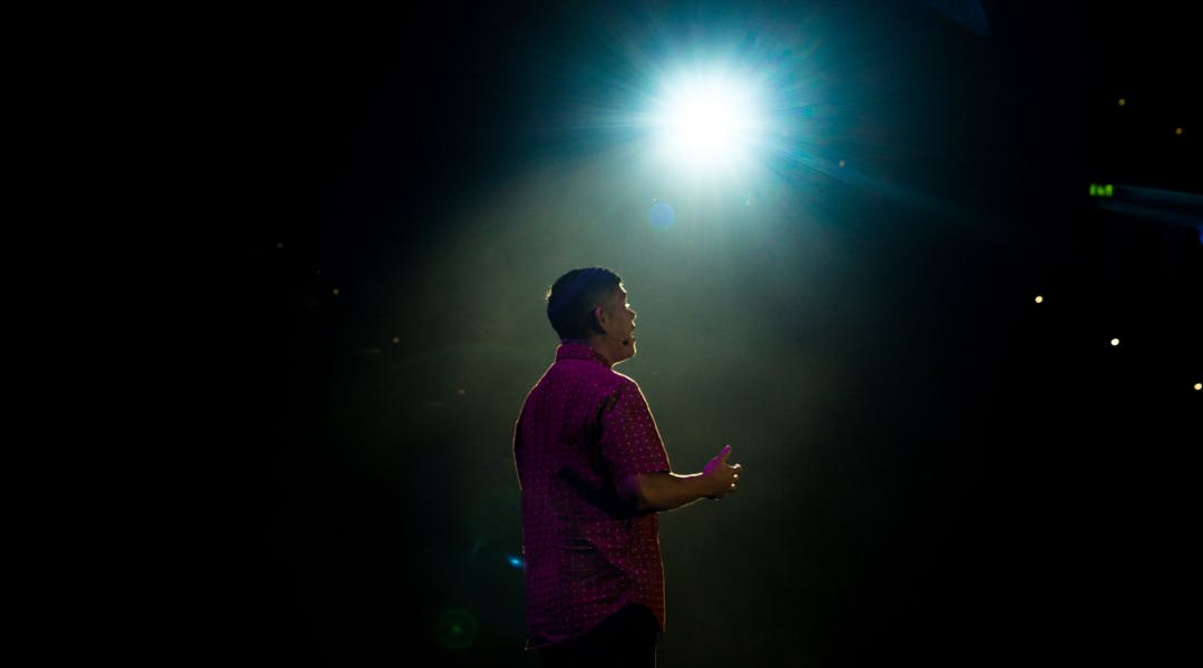 A spotlight casting a rim light on a man speaking on stage.