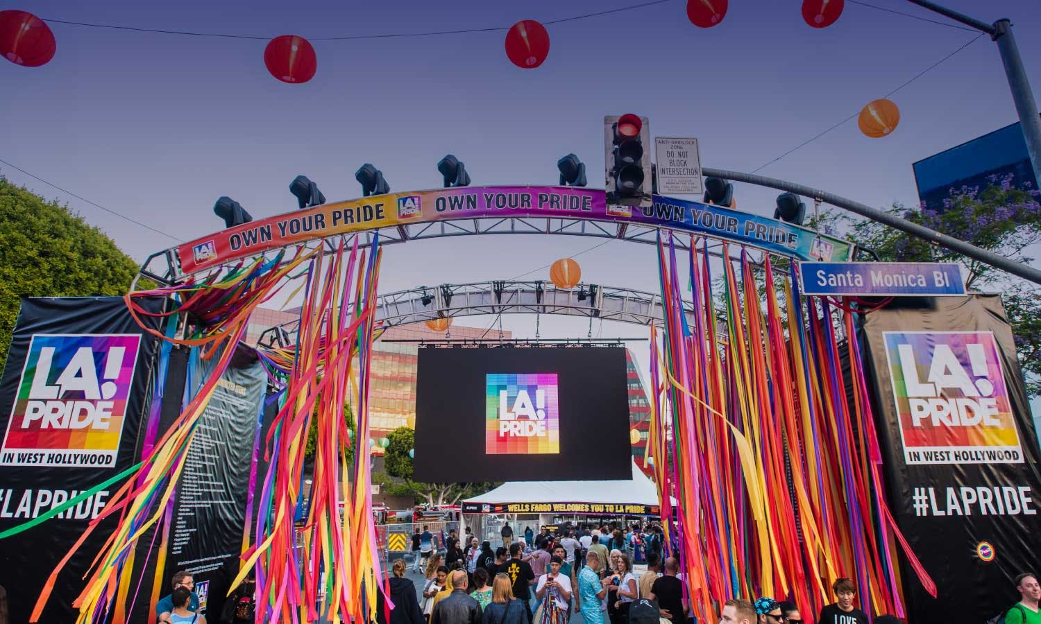 An archway of colorful streamers and Chinese lanterns at LA's Pride Parade with people underneath the arch