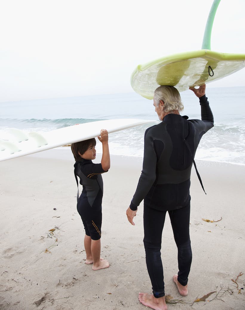 Two surfers, an elderly man and a child, hold their surfboards and size up the waves. 