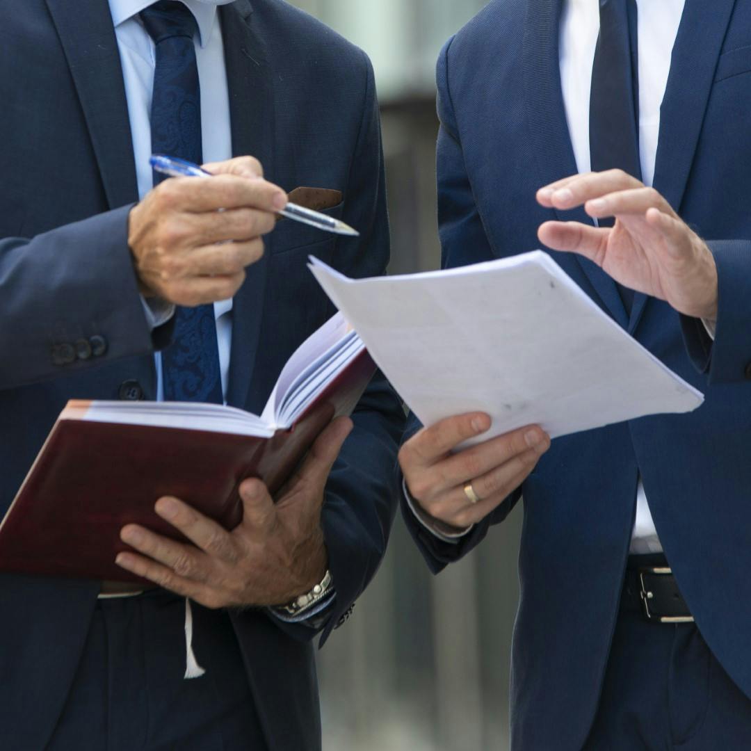 2 men in suits pointing at paperwork