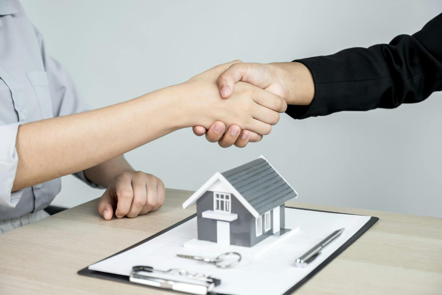 people shaking hands over a model house, keys and contract