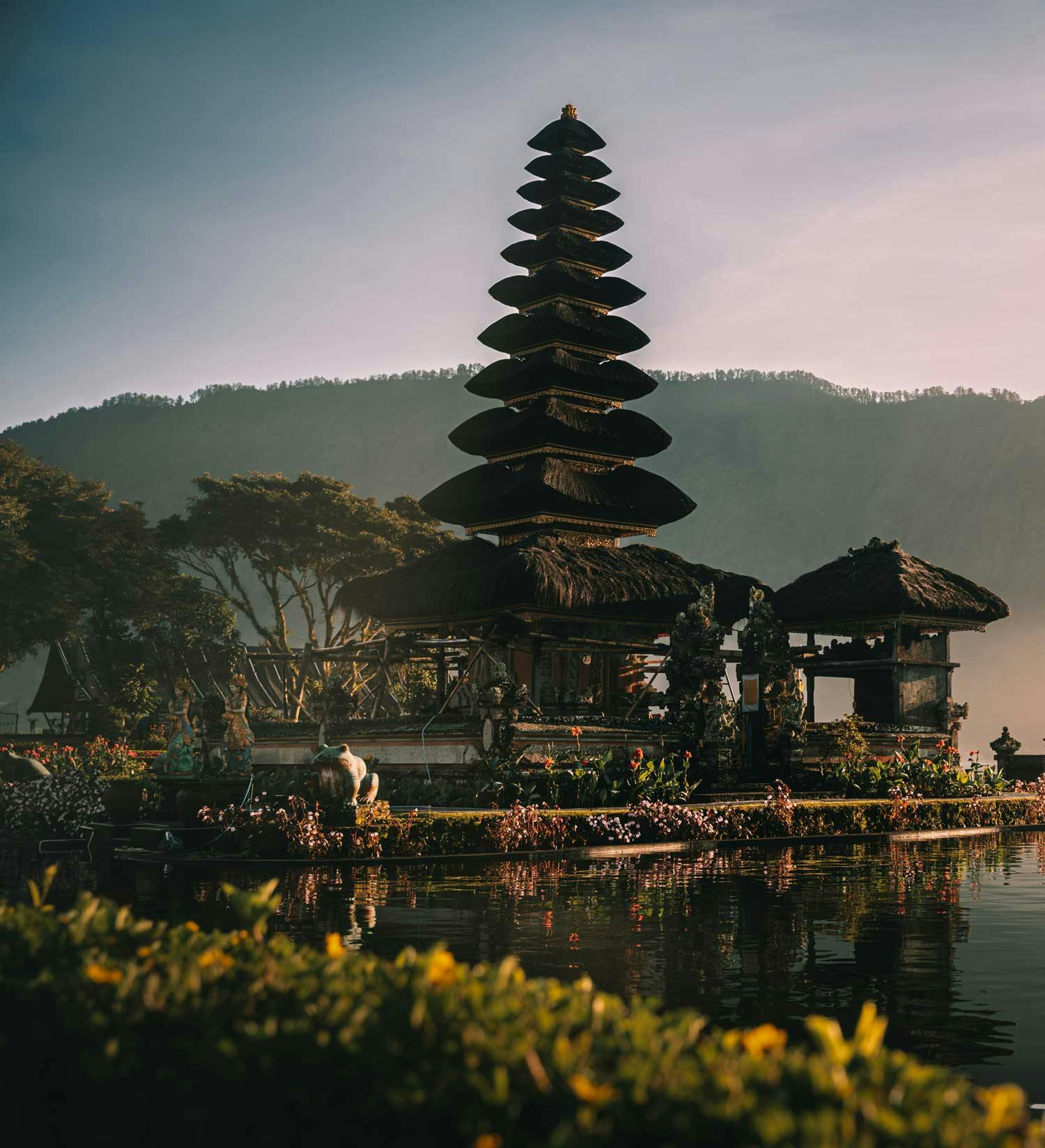 Pura Ulun Danu Bratan water temple at golden hour, reflected in the misty calm lake with forested mountains in the background