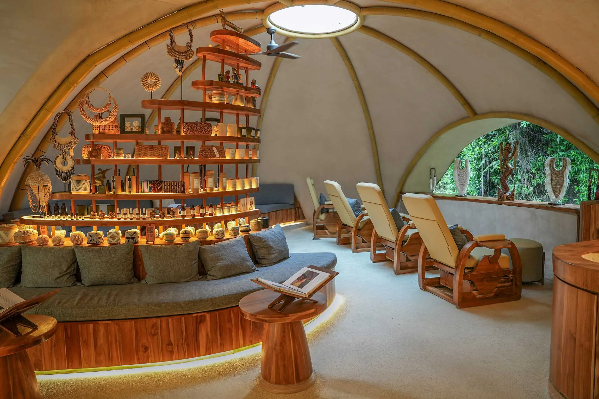 Luxurious Bali spa relaxation lounge featuring bamboo dome architecture, teak wood recliner chairs, glowing product shelves with natural skincare, and lush tropical garden views.