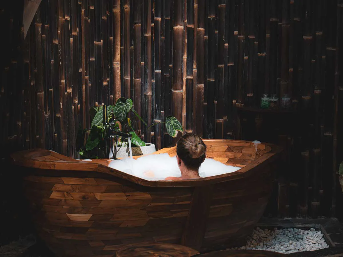 woman in a wooden bathtub enjoying a bubble bath in luxurious bathroom of an eco luxury resort in bali