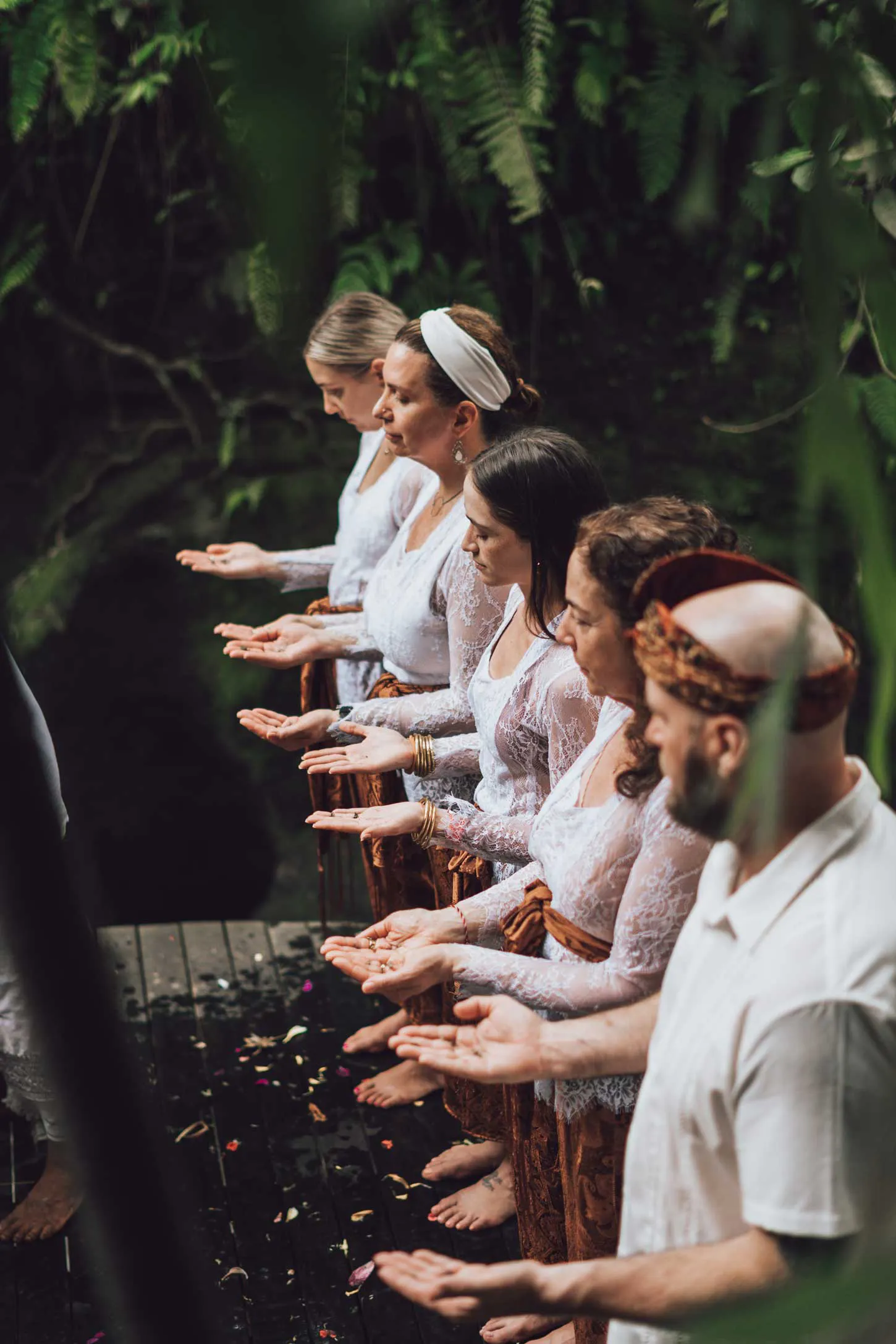 Retreat participants in traditional Balinese batik sarongs standing during a sacred ceremony at a lush jungle retreat venue in Bali