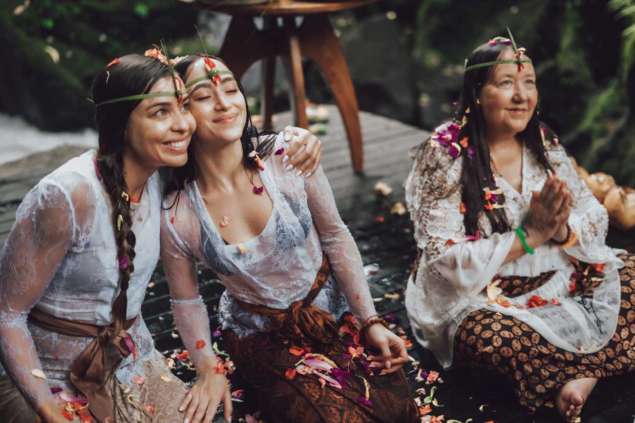 Smiling women adorned with tropical flower crowns after a Balinese purification ritual at a beautiful retreat venue in Bali