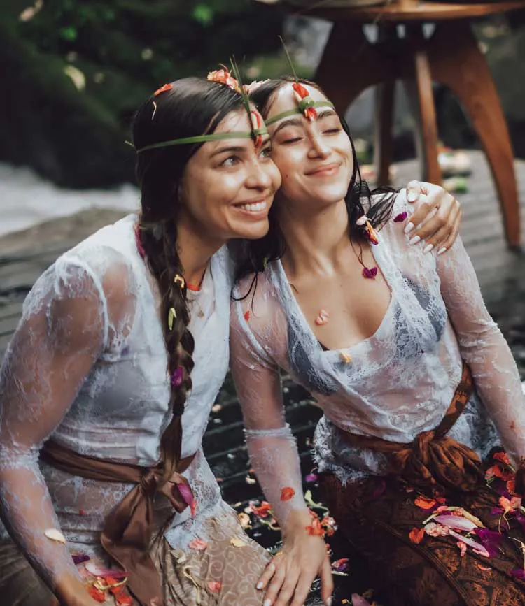 Smiling women adorned with tropical flower crowns after a Balinese purification ritual at a beautiful retreat venue in Bali