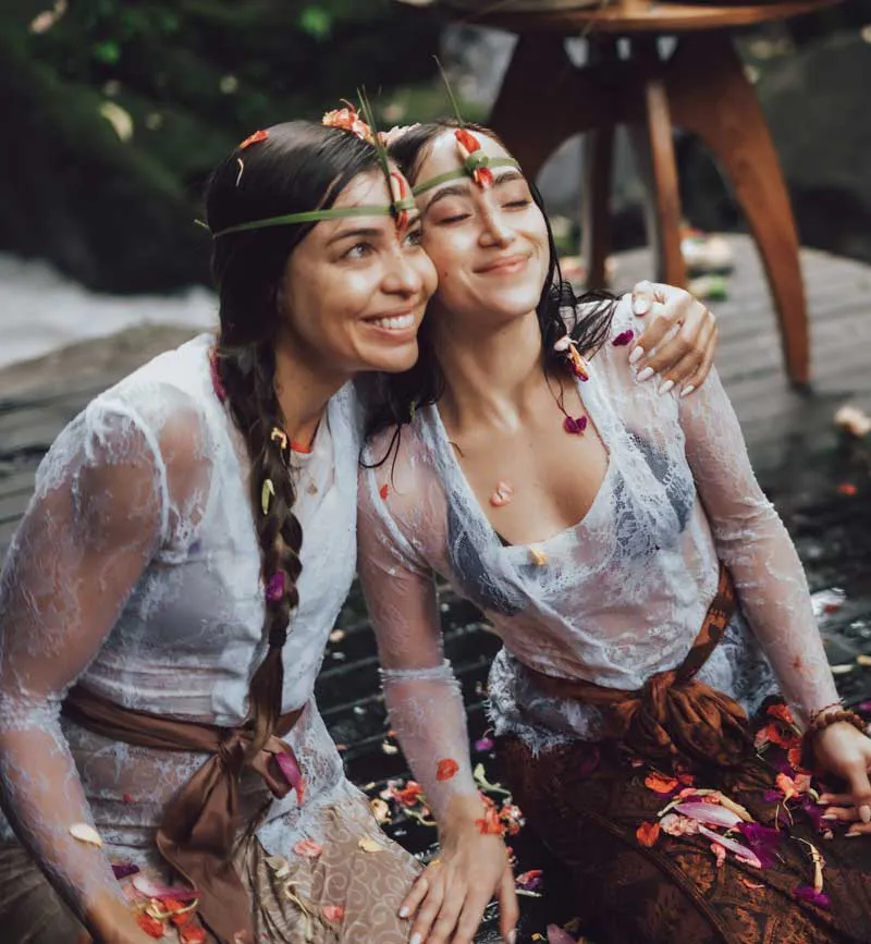 Smiling women adorned with tropical flower crowns after a Balinese purification ritual at a beautiful retreat venue in Bali