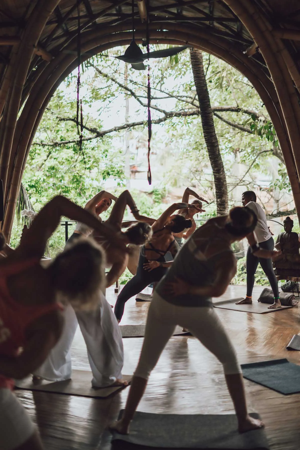 Group yoga class in a stunning open-air bamboo yoga shala surrounded by tropical jungle at a Bali retreat venue