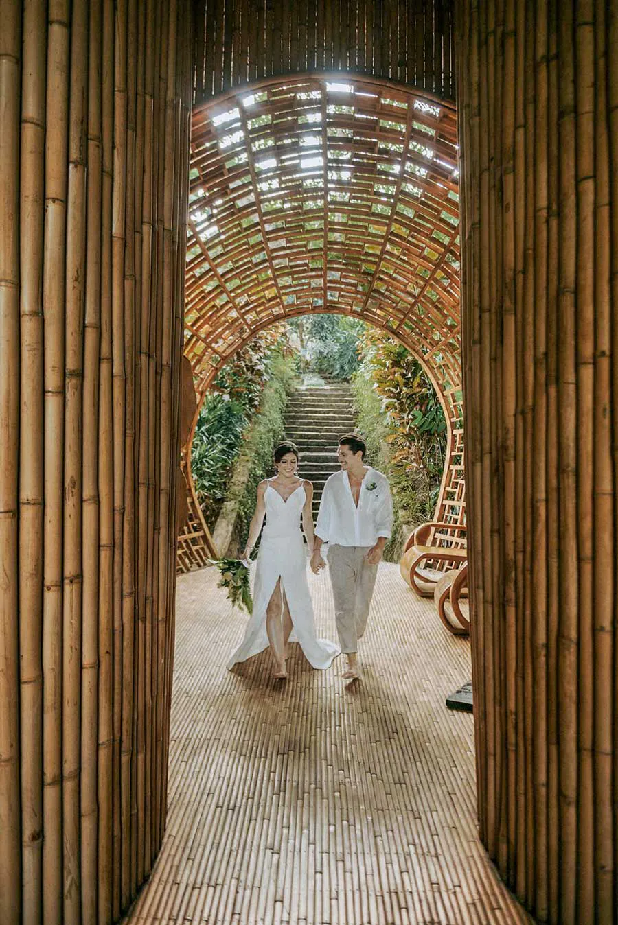 Happy couple strolling through a dramatic bamboo tunnel corridor at a luxury eco-friendly wedding venue in Bali, Indonesia