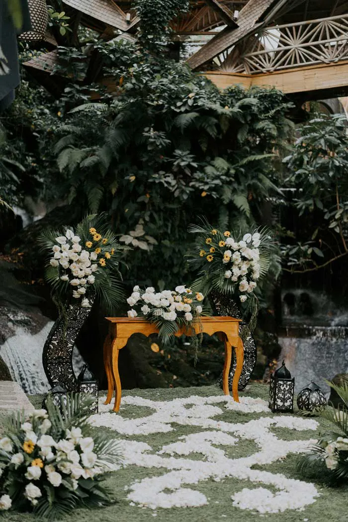Intimate garden wedding altar with white roses, yellow flowers, set beside a waterfall in Ubud Bali