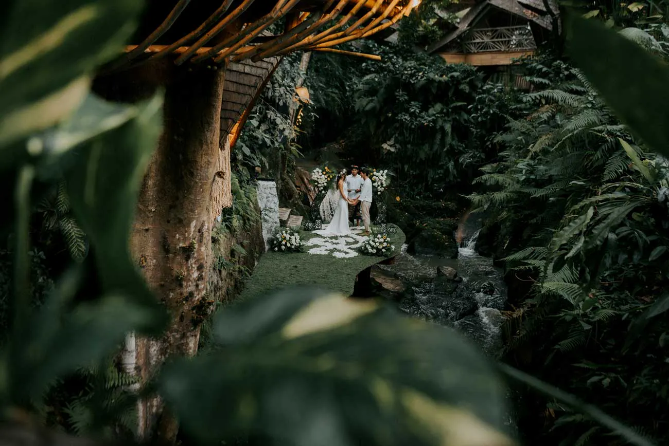 Intimate outdoor jungle wedding ceremony framed by tropical ferns and a flowing river at a hidden eco wedding venue in Ubud Bali
