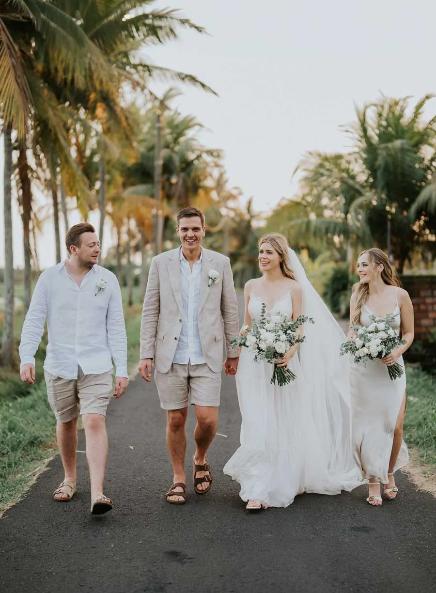 Guests walking along a palm tree-lined road in Bali at golden hour, casual tropical destination wedding style