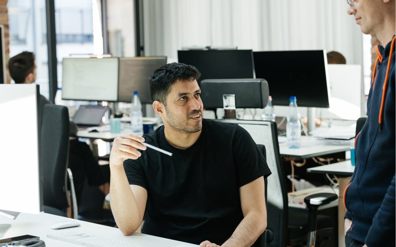 Der Ingenieur für Software Arthur Santana bespricht etwas mit dem Ingenieur für maschinelles lernen Ronald Richter an seinem Schreibtisch.