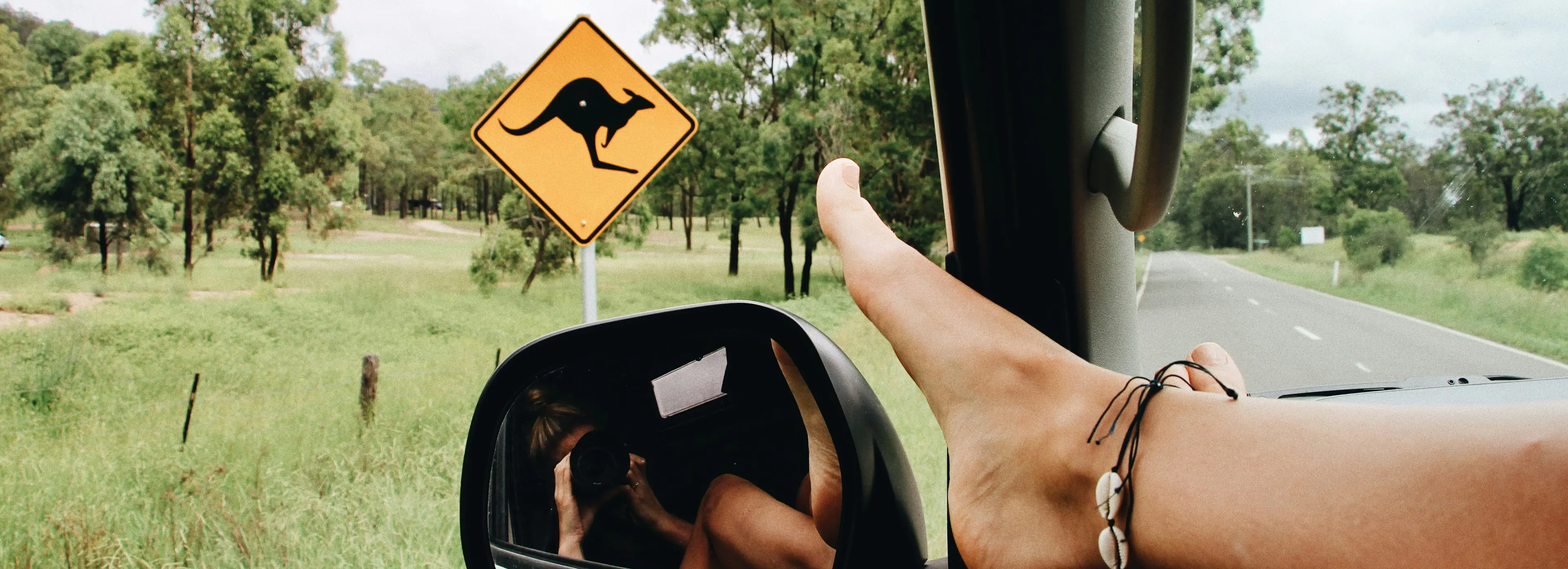 Young girl enjoying a road trip in their car taking a selfie that also shows a warning kangaroos ahead sign