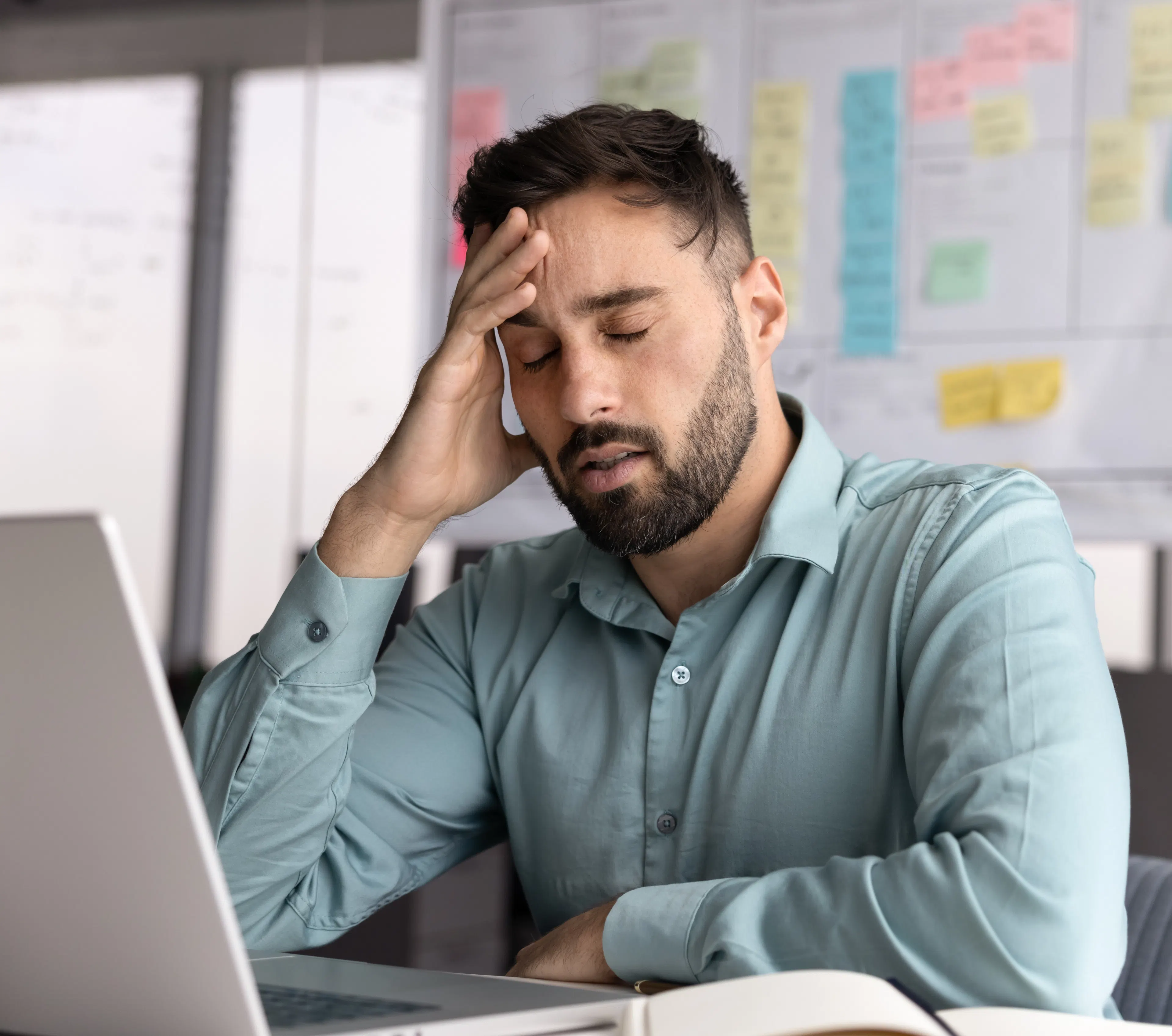 Stressed tired young businessman sit at workplace before notebook with closed eyes feel exhausted from information overload suffer headache concentration loss