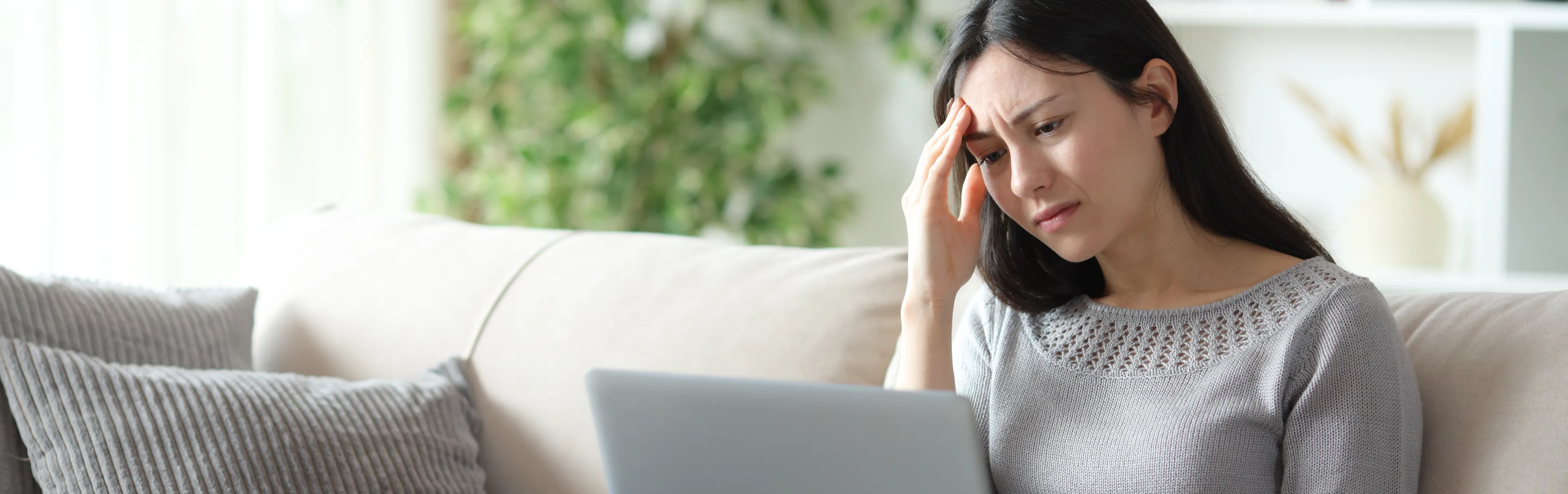 Worried woman frustrated about a rejected loan application from a bank sitting on a couch at home with a laptop