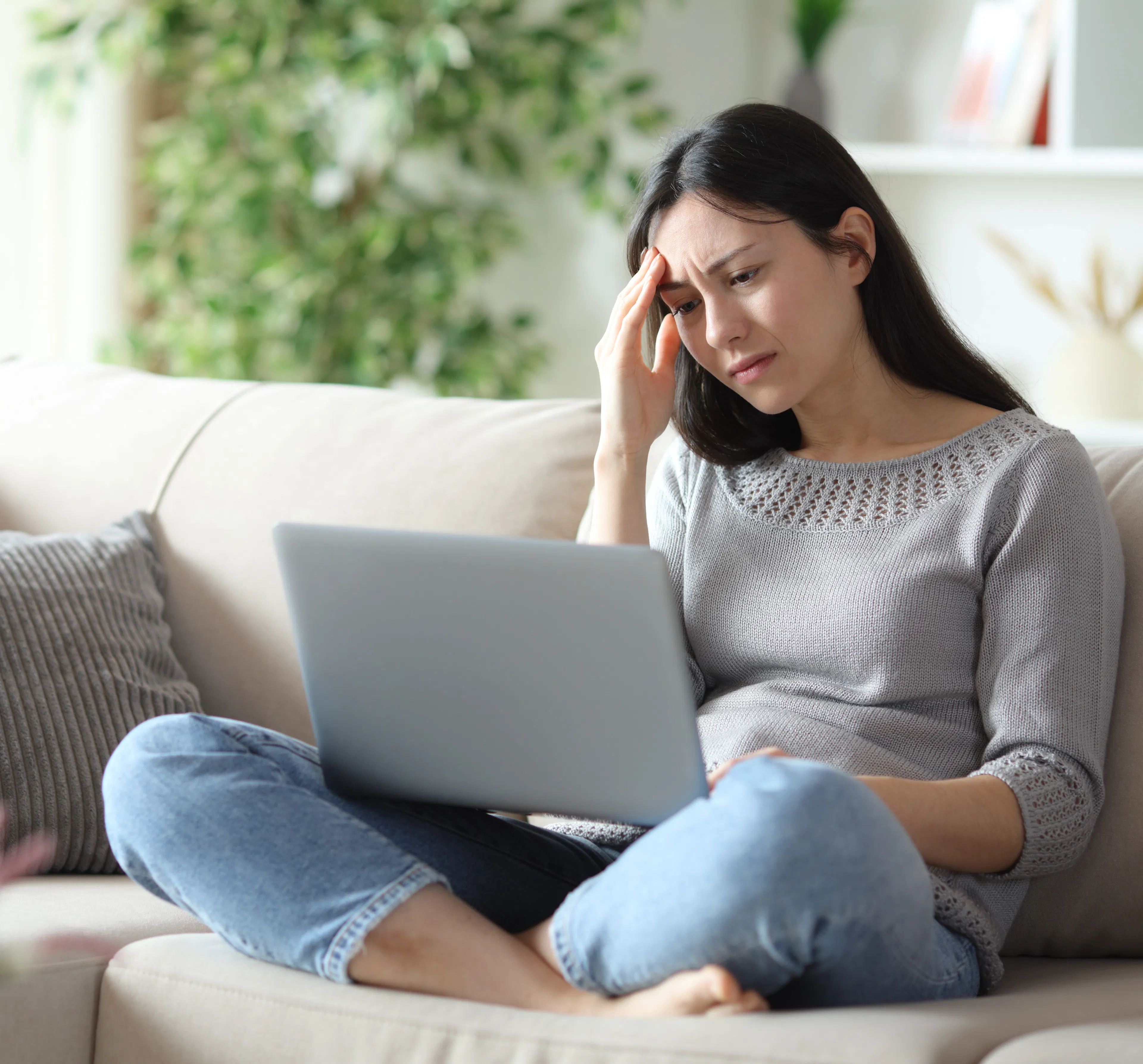 Worried woman frustrated about a rejected loan application from a bank sitting on a couch at home with a laptop