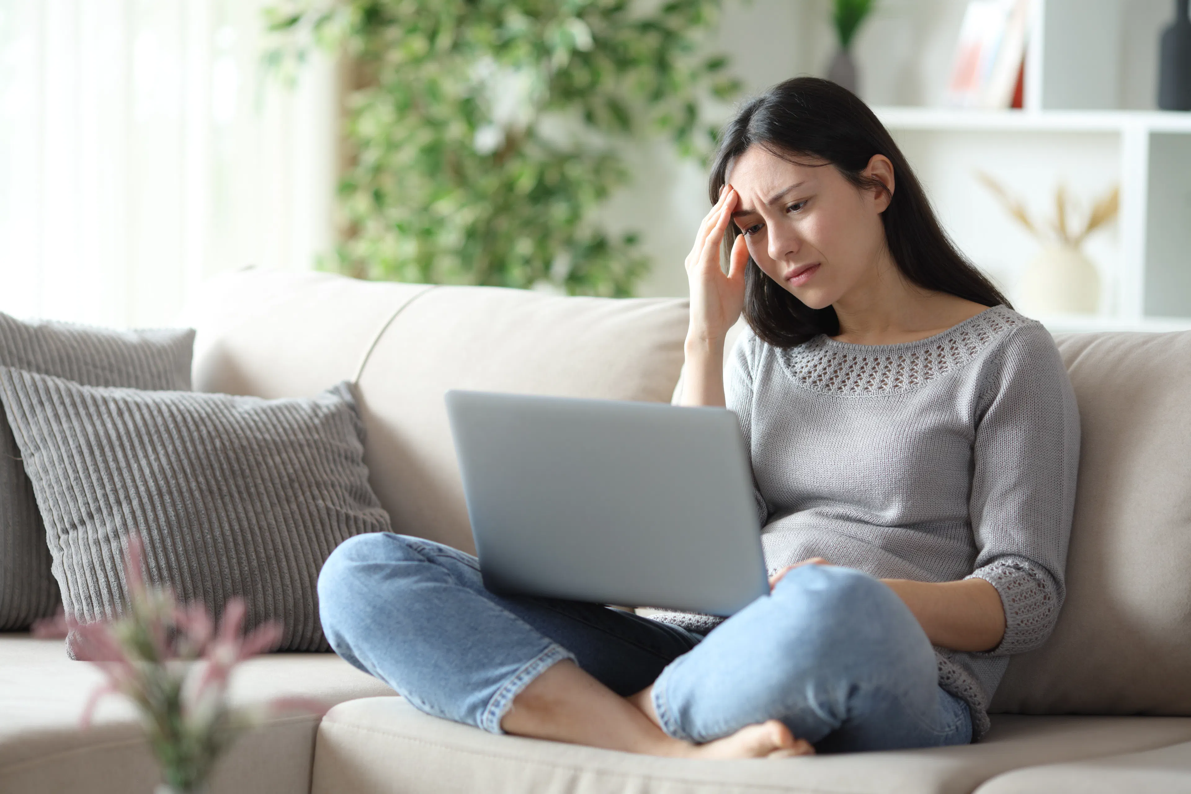 Worried woman frustrated about a rejected loan application from a bank sitting on a couch at home with a laptop