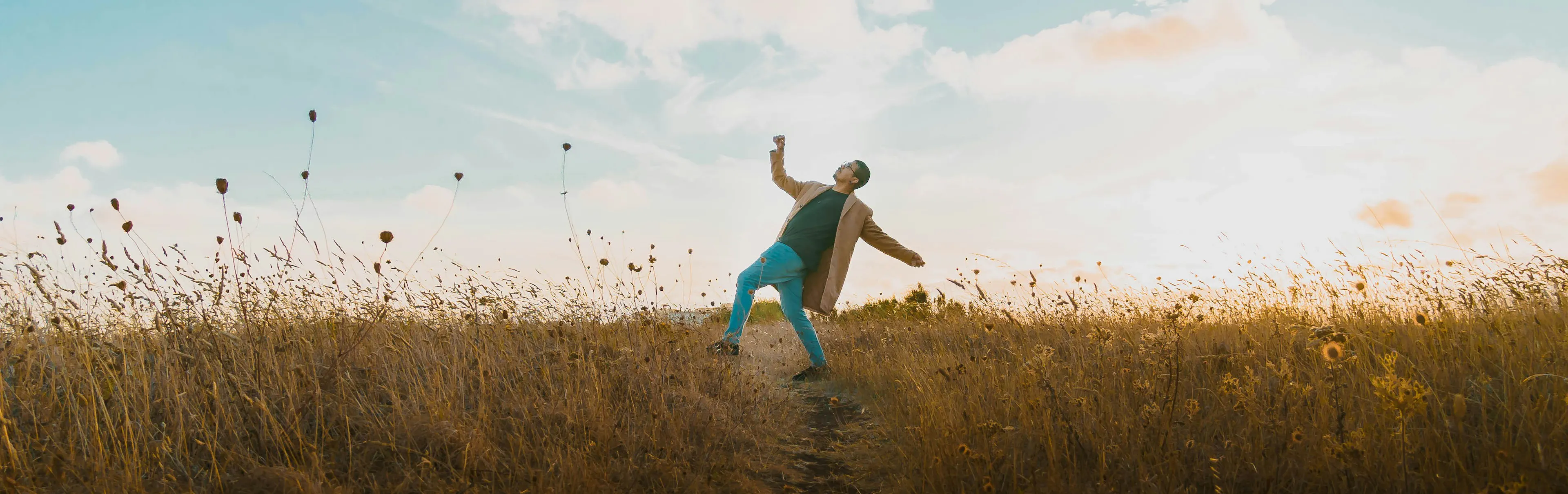 Person dancing in a grass field with a sunset in the background