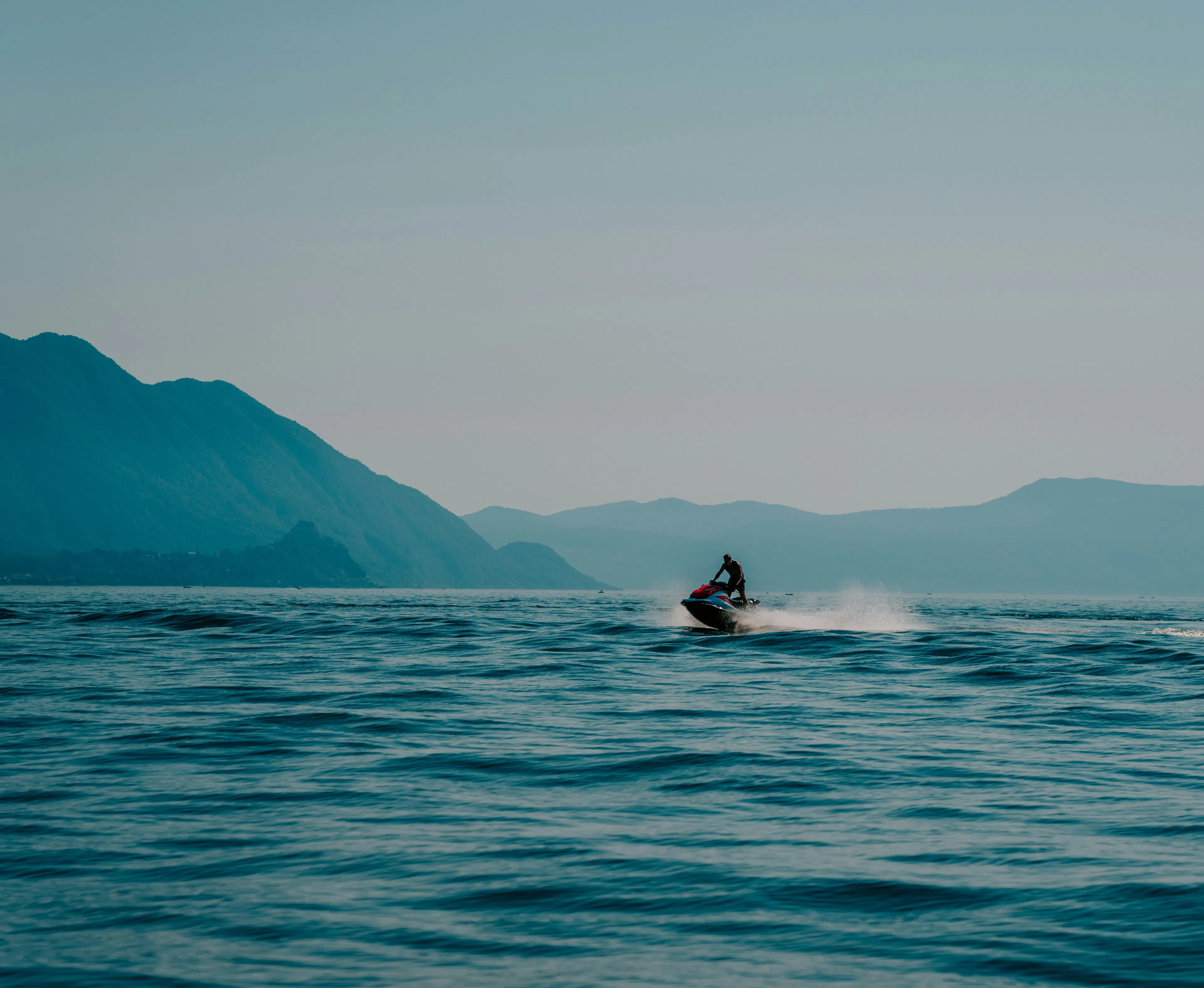 person driving a jet sky in a blue sea with mountains in the background