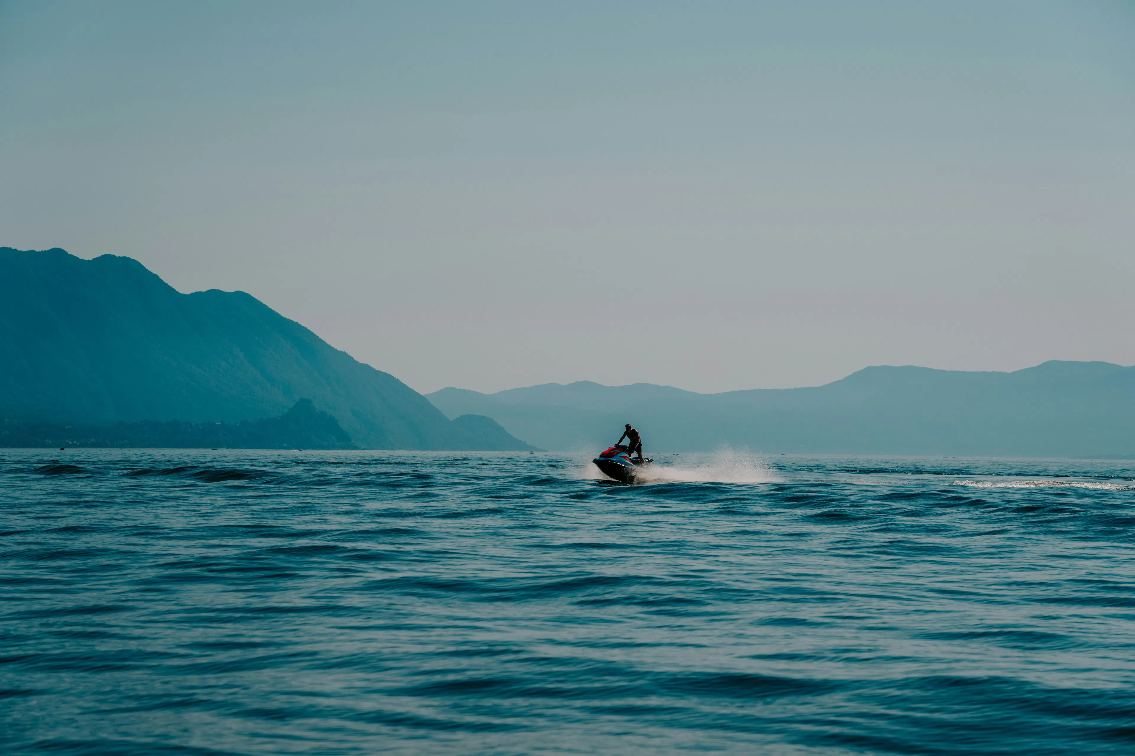 person driving a jet sky in a blue sea with mountains in the background