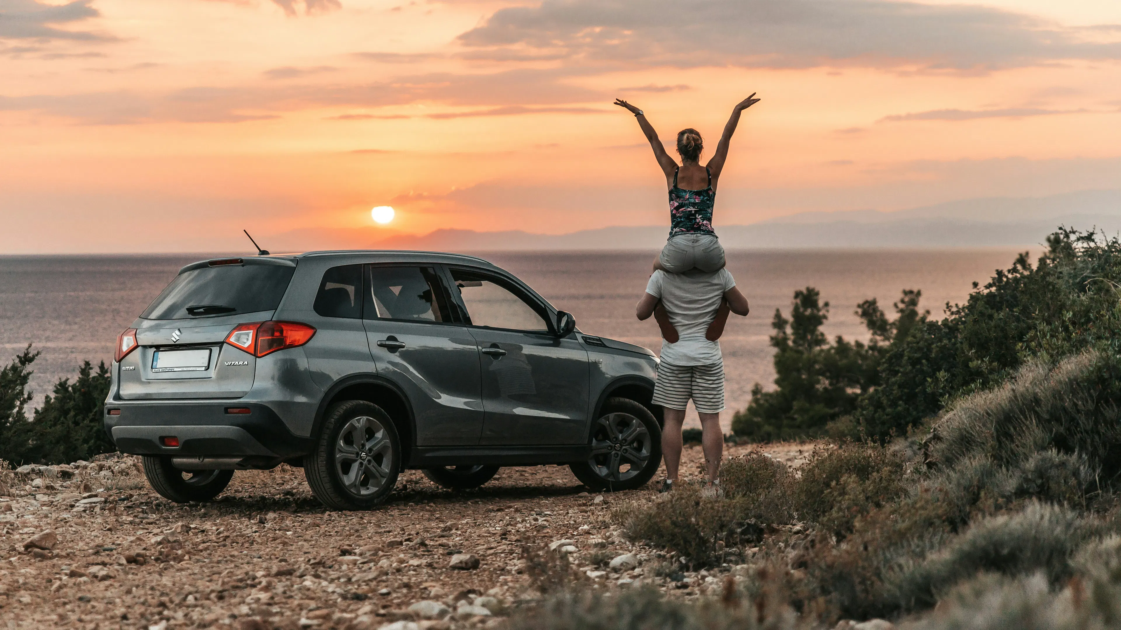 Young couple celebrating life next to their new car in a beach while watching the sunset
