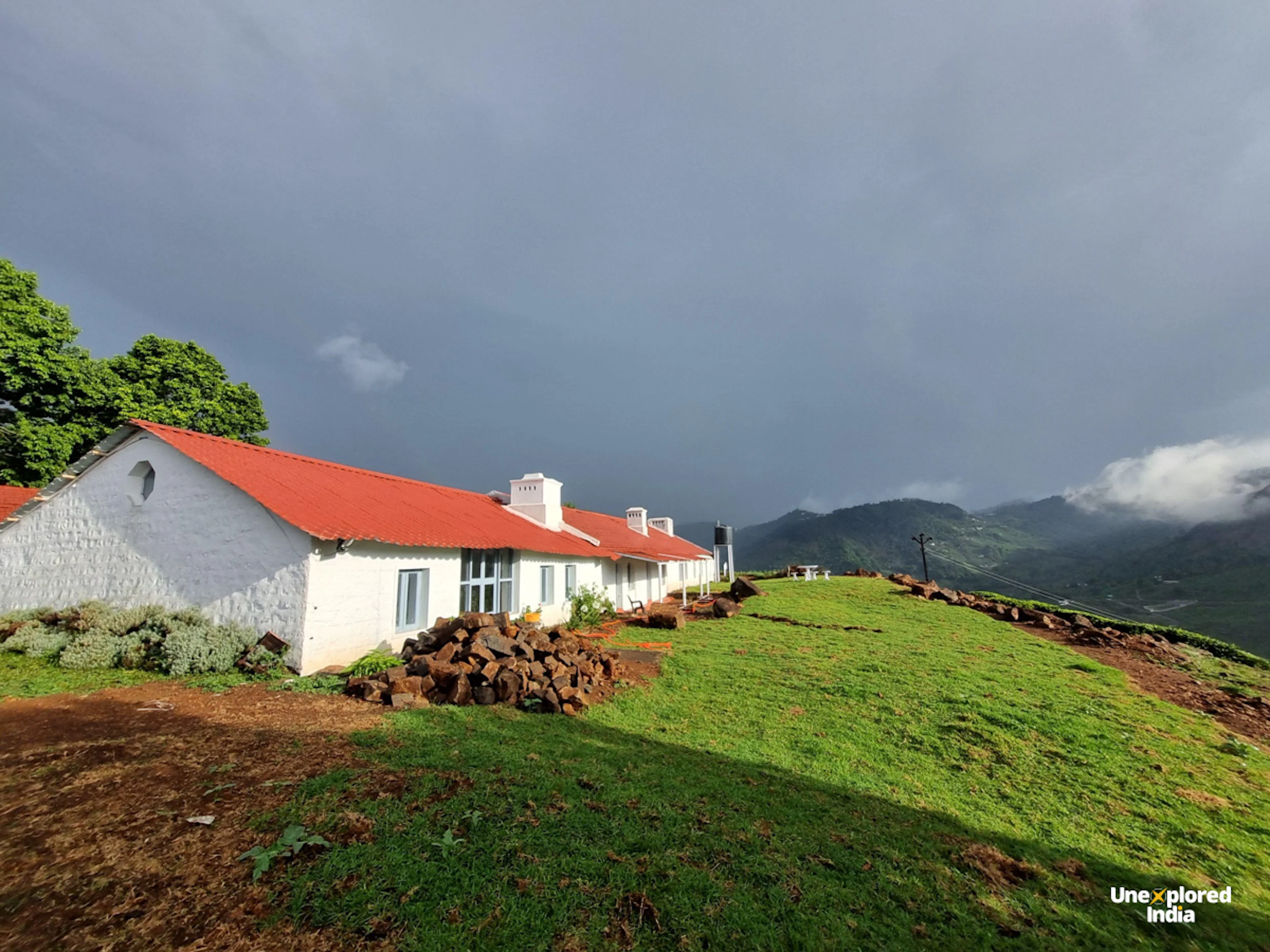 Orange-roofed homestay on a lush green hillside in Kotagiri, with mist-covered Nilgiri mountains stretching across the background.