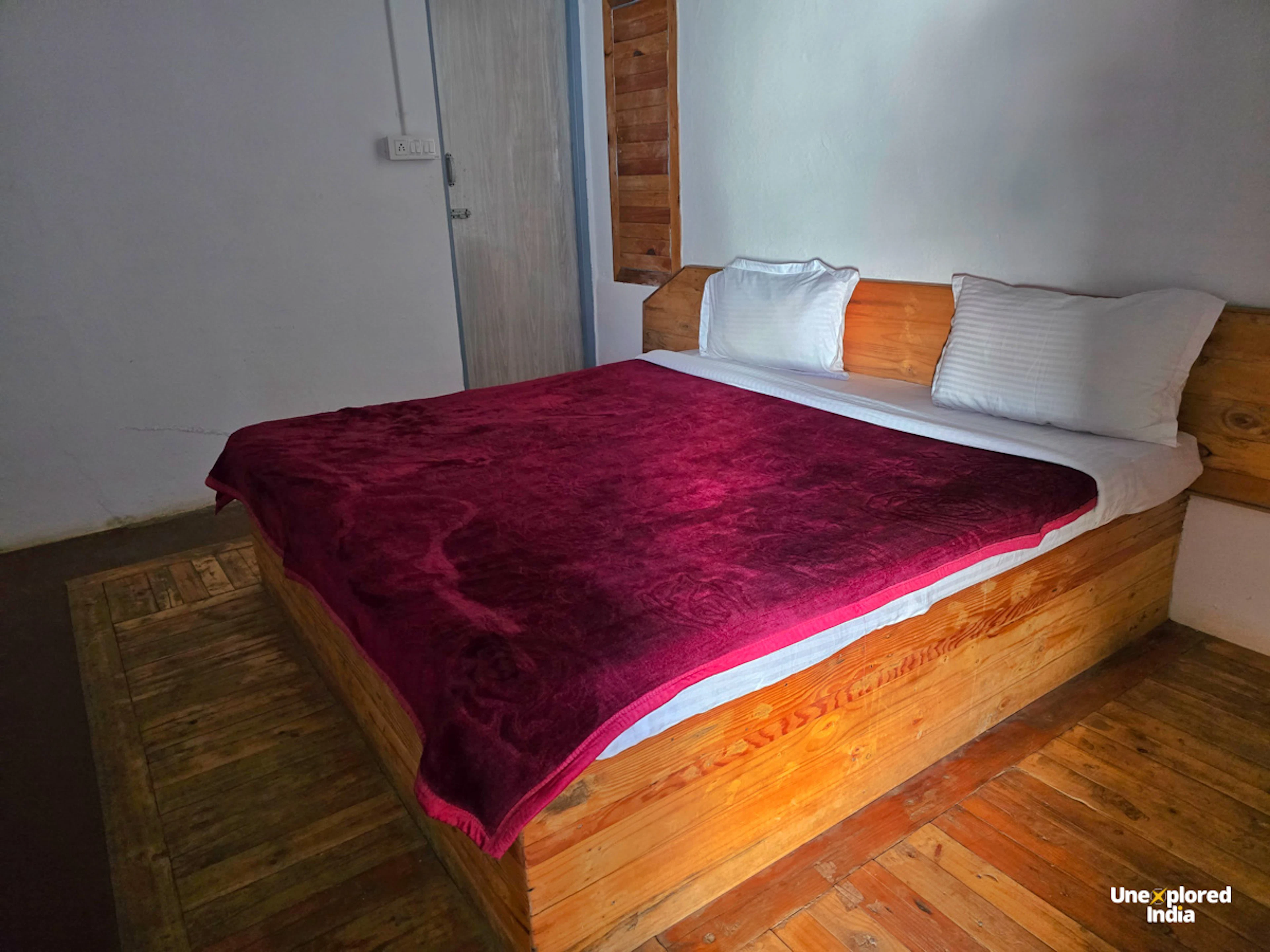 Wooden bedroom with a double bed and red blanket in a cosy Kotagiri stay in the Nilgiris.