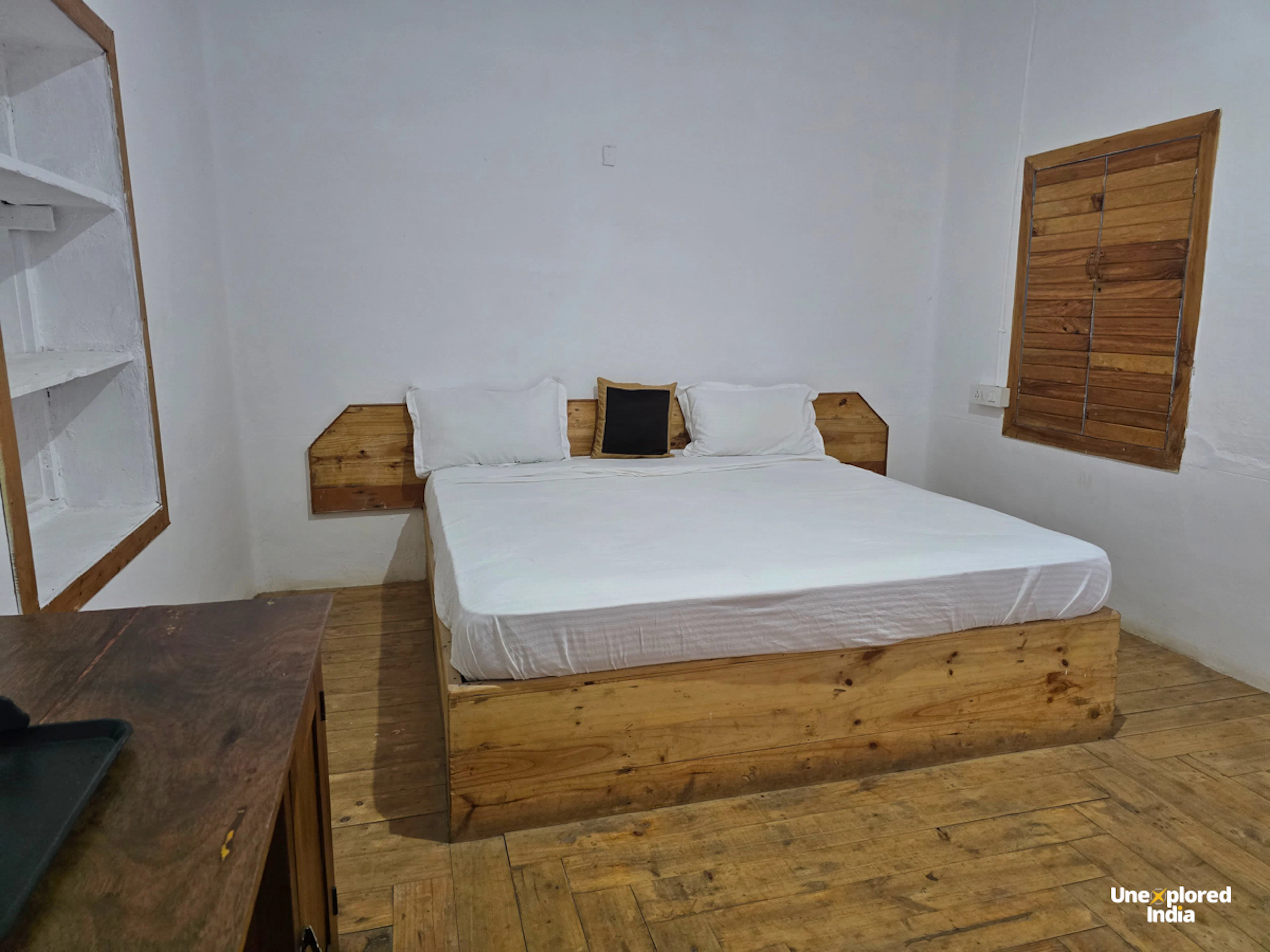 Wooden bedroom inside a cosy Kotagiri stay in the Nilgiris, with a double bed, wooden flooring and shuttered window.