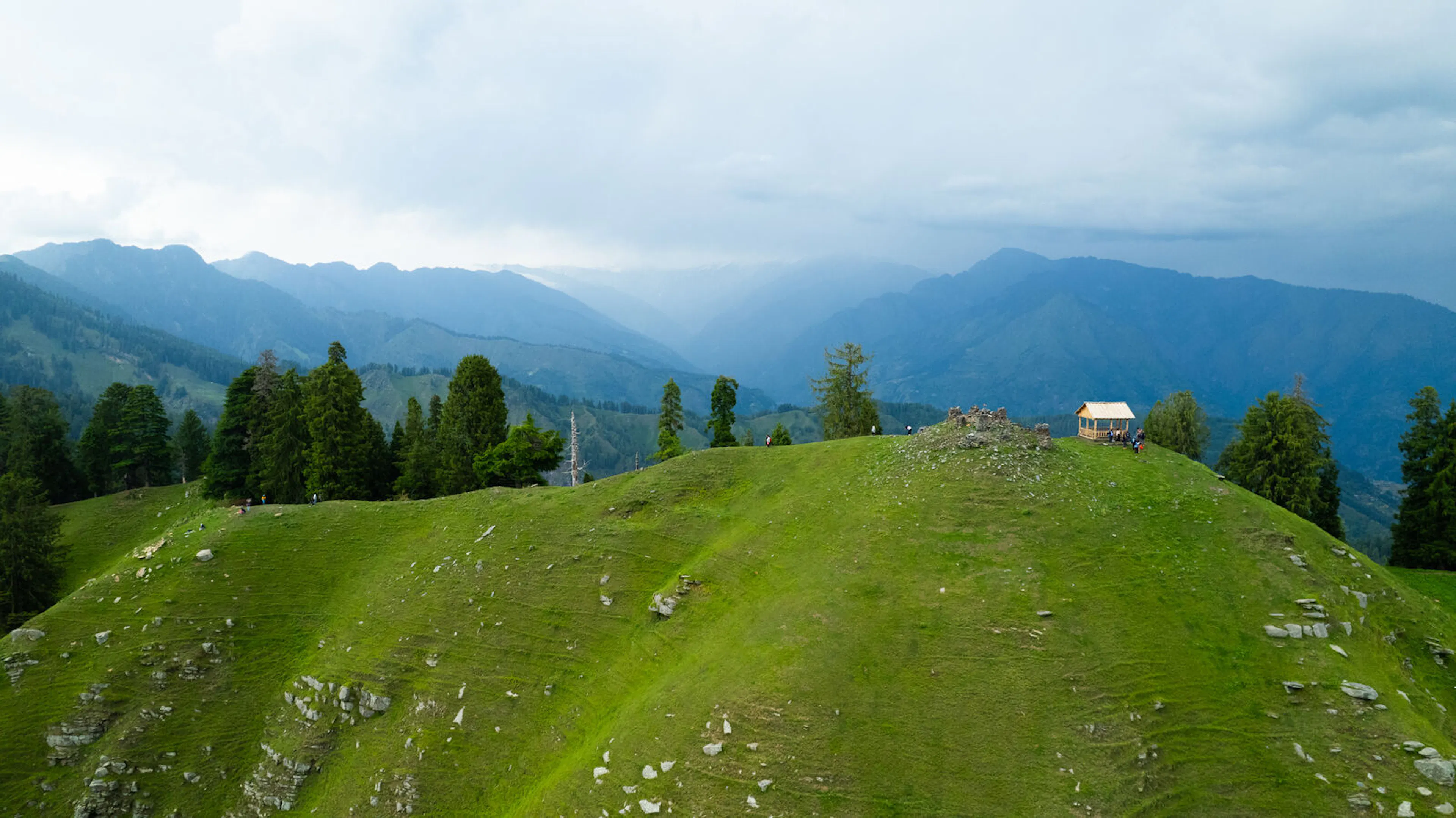 Himachal Pradesh villages and grasslands near Kaisdhar, with mountain temple architecture and Dhauladhar range views