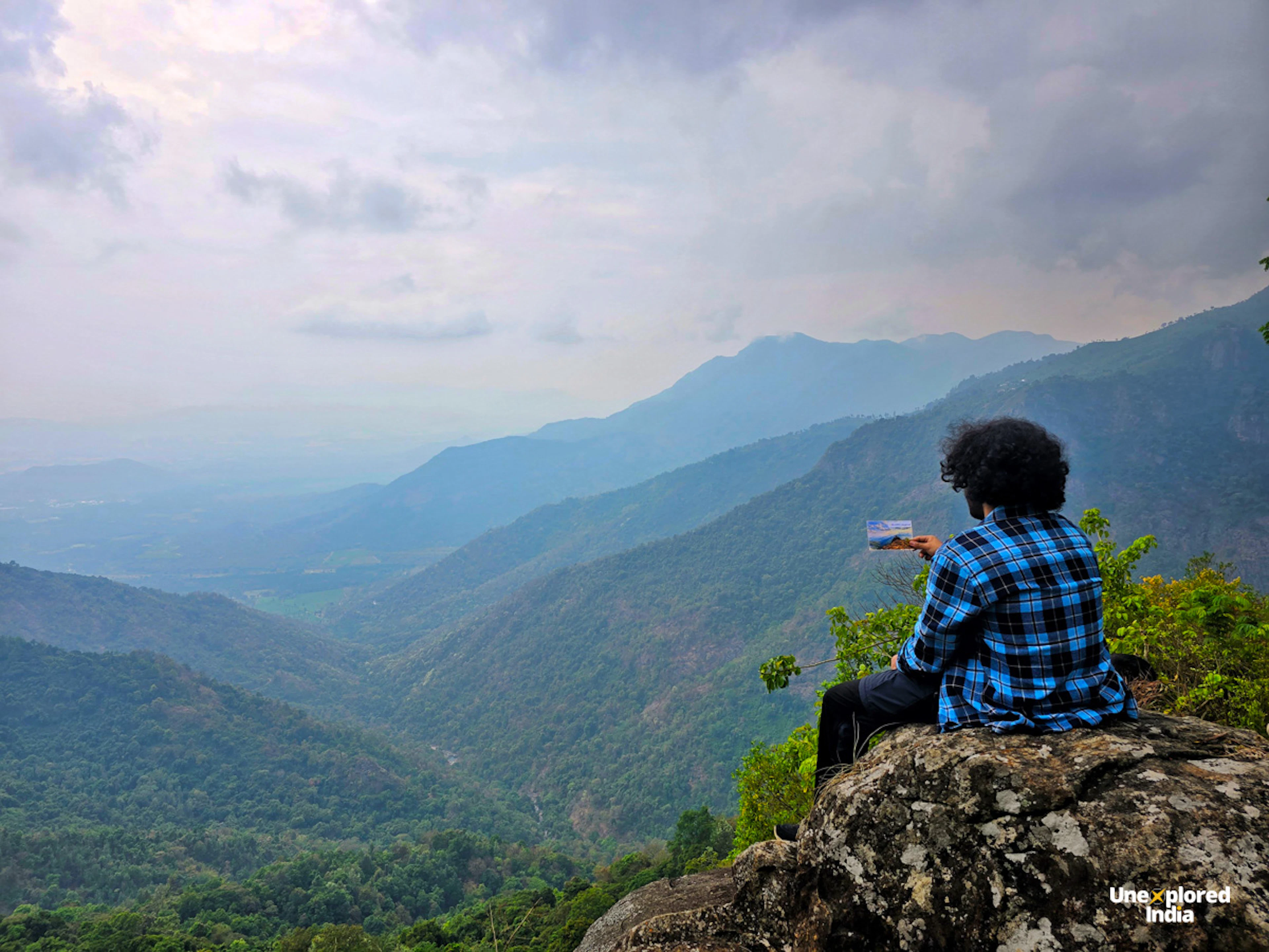 Person sitting on a cliff edge overlooking the Nilgiris hills and shola forests