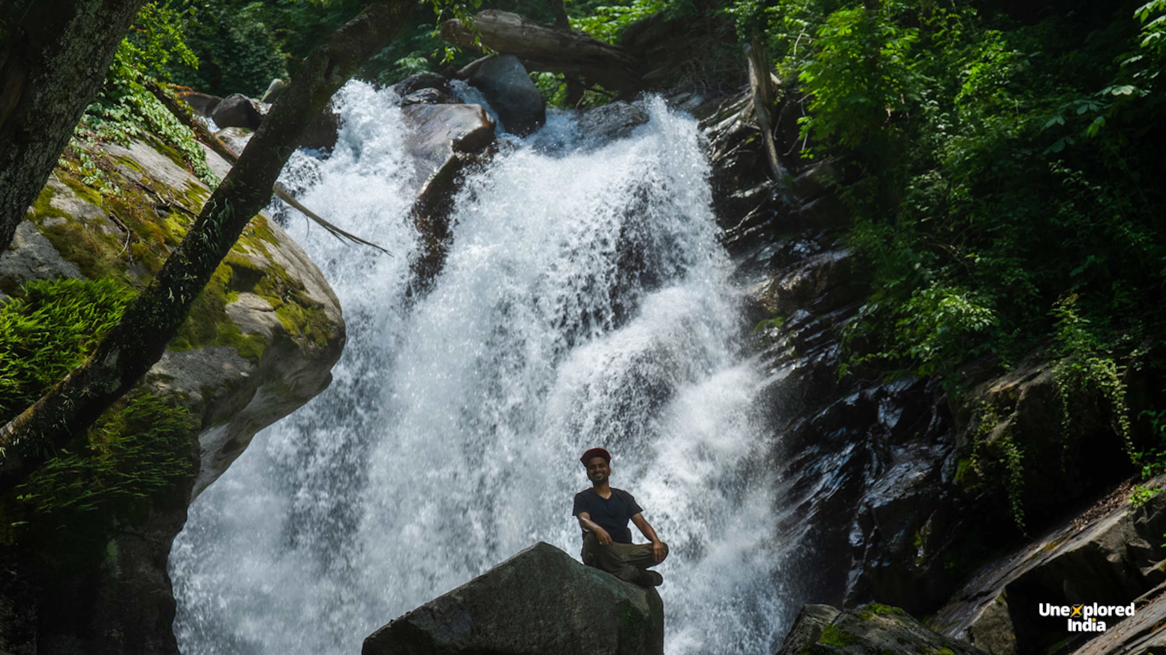 a person sitting on a stone in front of a cascading waterfall