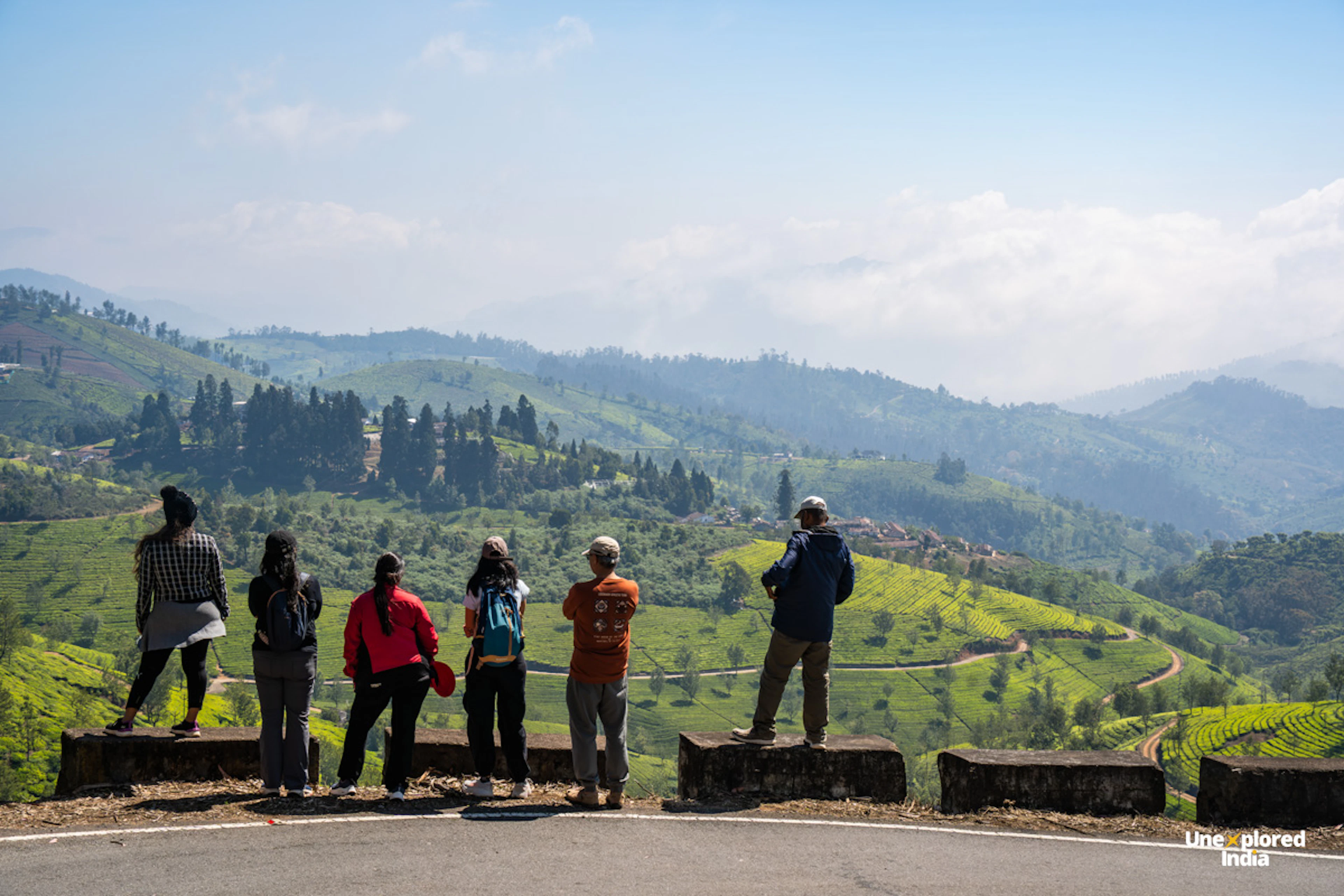 Six people overlook lush tea estates Ooty across the rolling green hills of the Nilgiris from a roadside viewpoint.