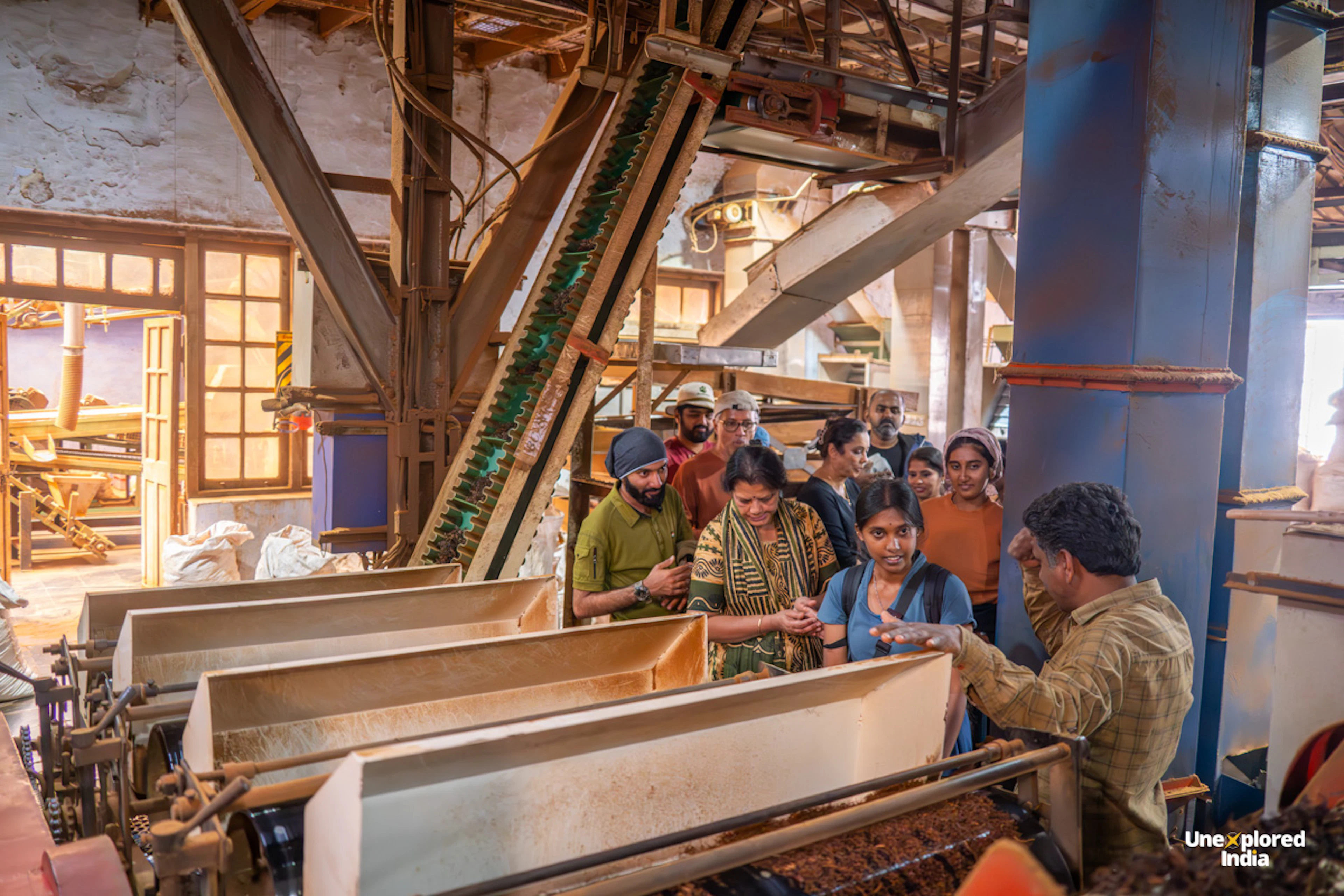 Visitors learn about tea processing machinery during a guided tour of a tea factory in the Nilgiris, surrounded by equipment.
