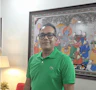 a man wearing a green shirt standing infront of a traditional painting