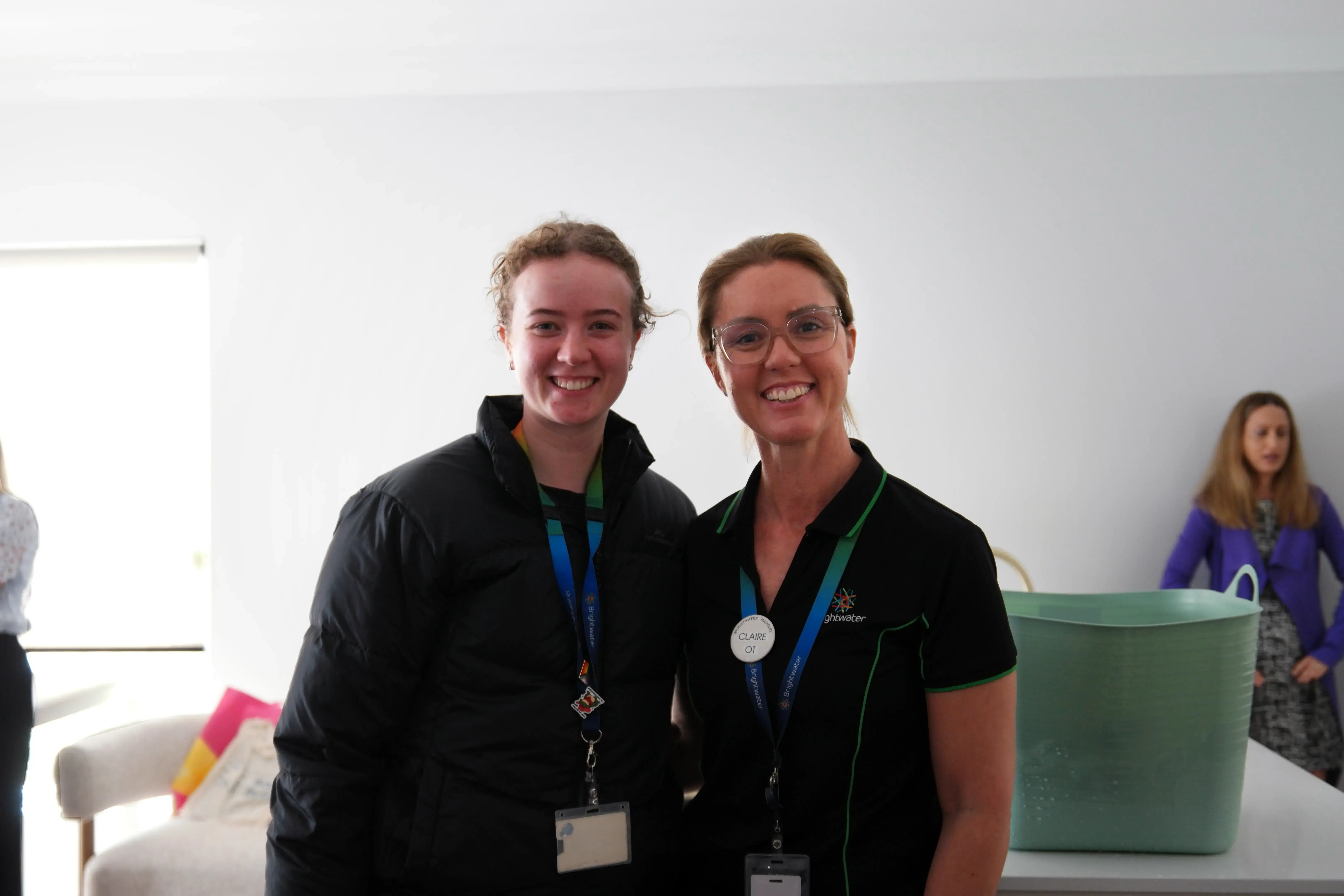 Two smiling attendees wearing name lanyards posing together at the Sana Living assistive technology education event.
