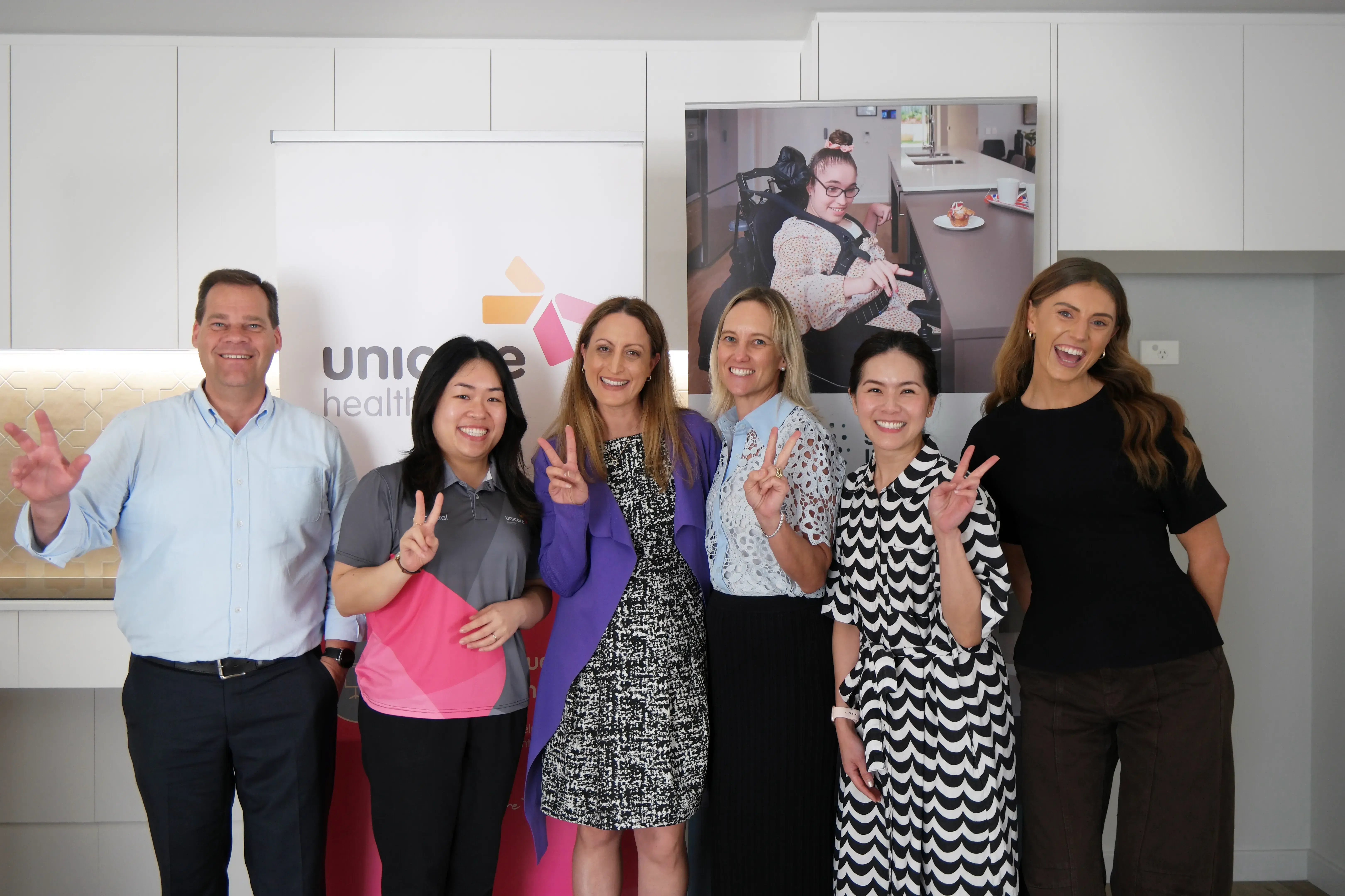 Six team members posing together in front of Unicare Health banners at the Sana Living education collaboration in Perth.