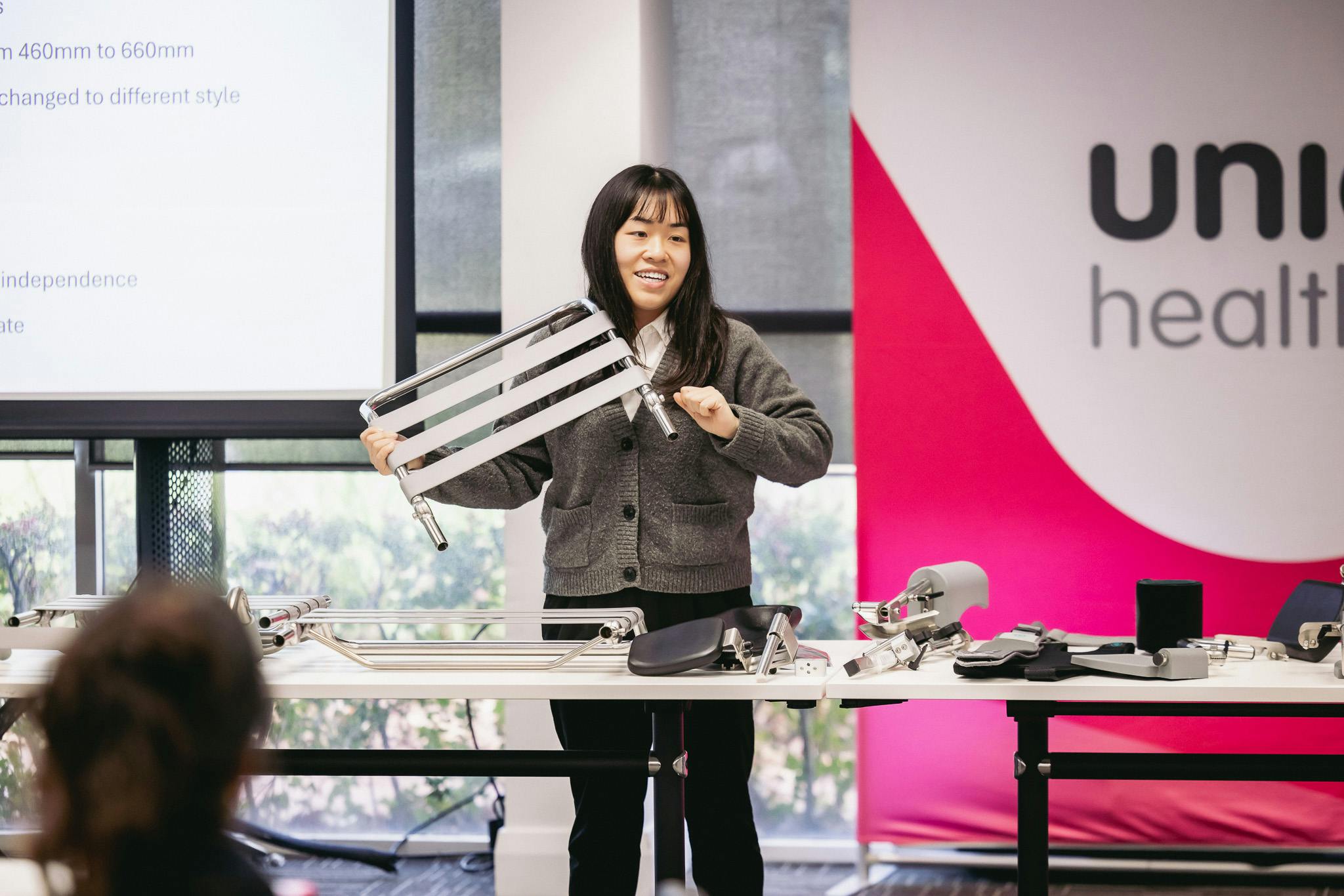 clinical educator holds up a removable shower commode backrest in front of a table of shower commode accessories